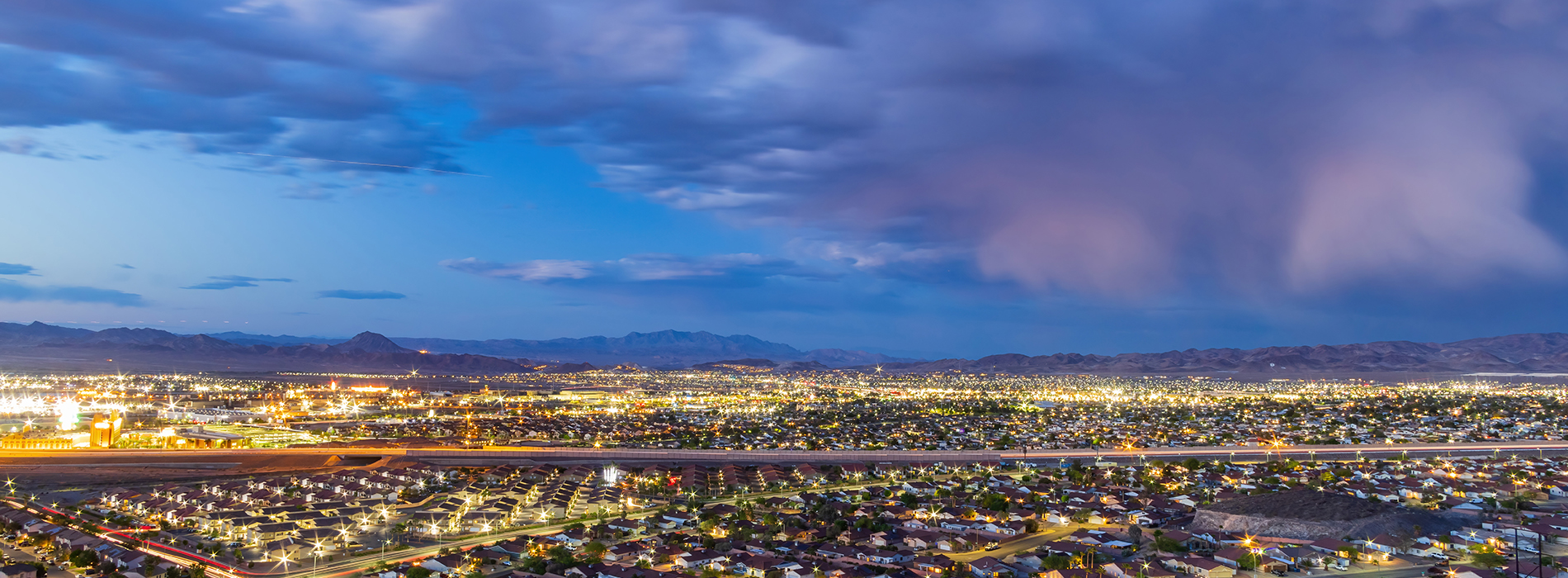 The image depicts a city skyline at twilight with a prominent lighted sign, set against a backdrop of a dark blue sky with clouds and stars.