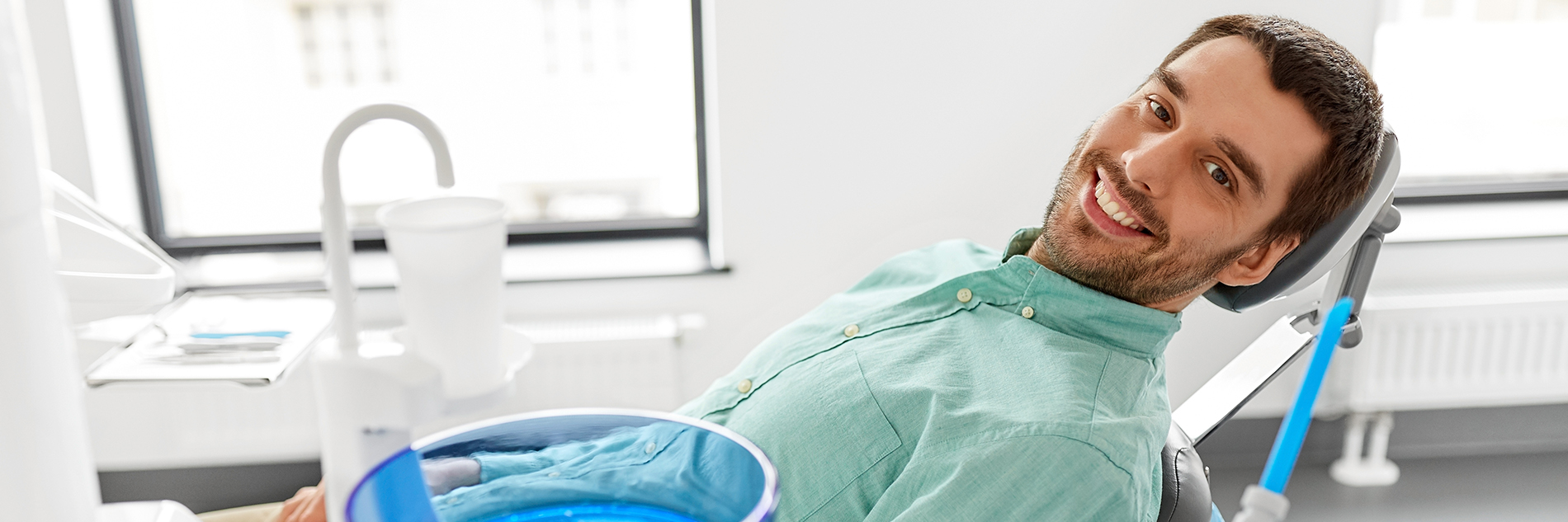 A man sitting in a dental chair with a blue tray on his lap, smiling and looking directly at the camera.